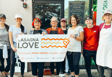 Eight people stand smiling holding a Lasagna Love banner