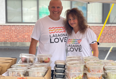 Man and woman standing before packaged food dressed in Lasagna Love t shirts
